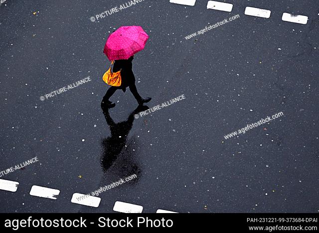 21 December 2023, North Rhine-Westphalia, Duesseldorf: A pedestrian crosses the street with her umbrella. People in North Rhine-Westphalia have to prepare for...