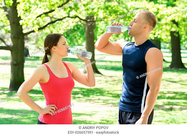 Young Athletic Couple Drinking Water After Exercise In Park