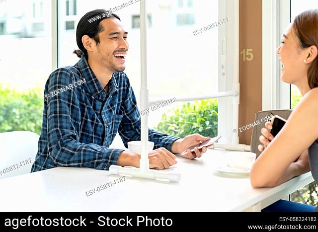 Asian young couple eating out together at new normal social distance restaurant with table shield partition reduce infection of coronavirus covid-19 pandemic