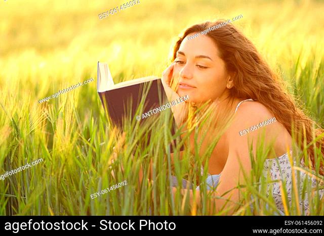 Woman reading a book relaxing sitting in a wheat field at sunset