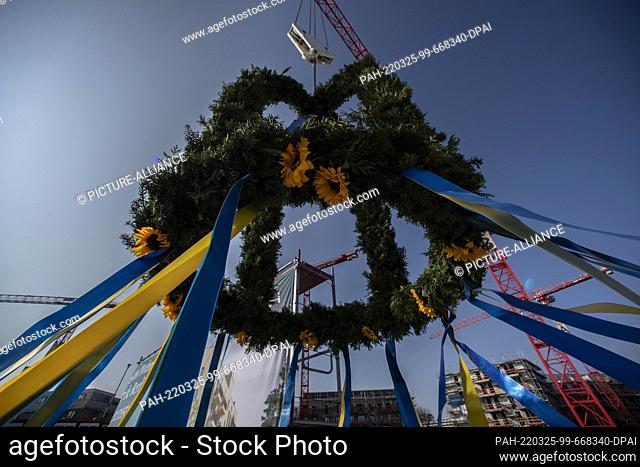 25 March 2022, Berlin: A topping-out wreath hangs from a crane at the topping-out ceremony for around 1, 000 apartments in Berlin's Siemensstadt district