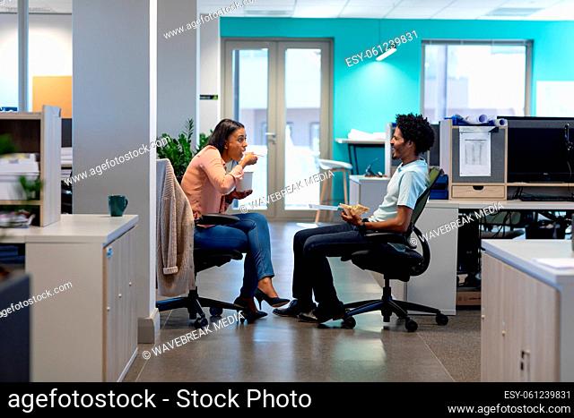 Multiracial professionals eating lunch together while sitting on chairs discussing at workplace
