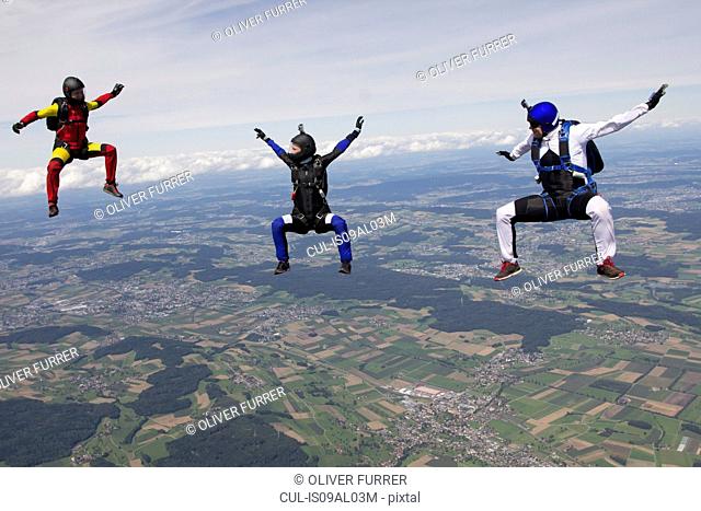 Team of three skydivers in sit fly position over Buttwil, Luzern, Switzerland