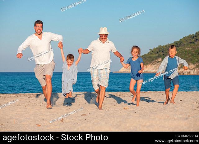 Happy family group of five, three generations are running along the beach