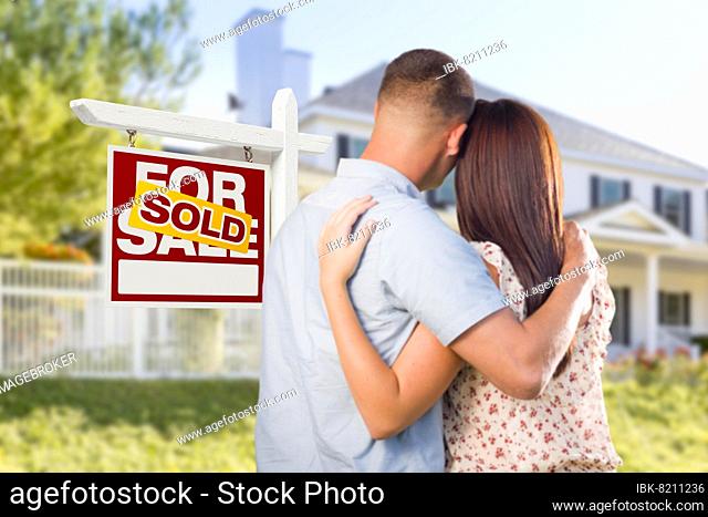 Sold for sale real estate sign and affectionate military couple looking at nice new house
