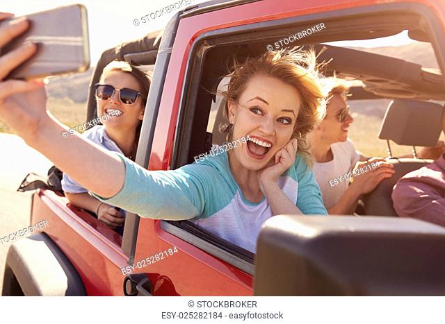Friends On Road Trip In Convertible Car Taking Selfie