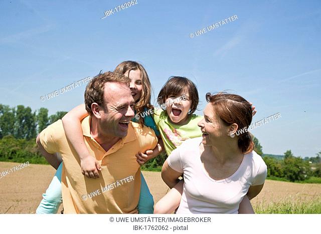 Mother and father carrying their children piggyback across a field