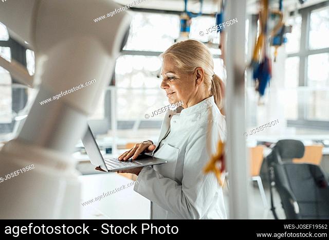 Smiling senior scientist using laptop in laboratory