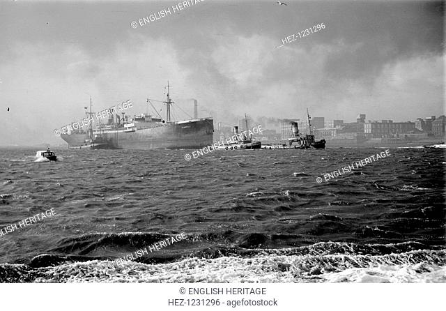 The 'Stanhill' is escorted by tugs, c1945-c1965. It passes outward bound along Woolwich Reach on the River Thames. It is clearly a windy day as waves can be...