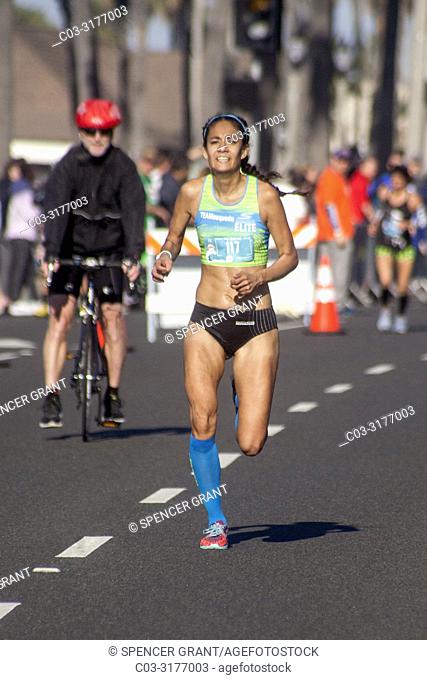 A Hispanic half marathon female winner nears the finish line on a street in Huntington Beach, CA. Note bicycle escort
