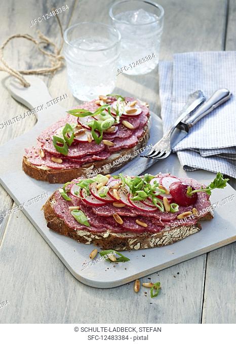 Two slices of bread with salami on a light wooden board