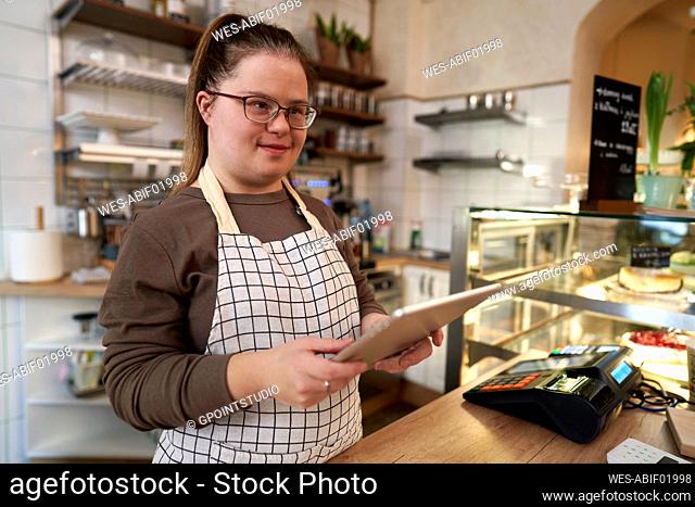 Smiling cafe owner with down syndrome standing with tablet PC