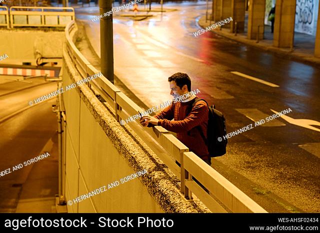 Businessman with backpack taking selfie with smartphone at night, Frankfurt, Germany