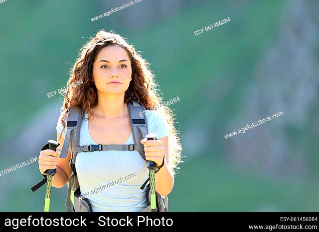 Front view portrait of a hiker woman walking in the mountain wih poles and backpack