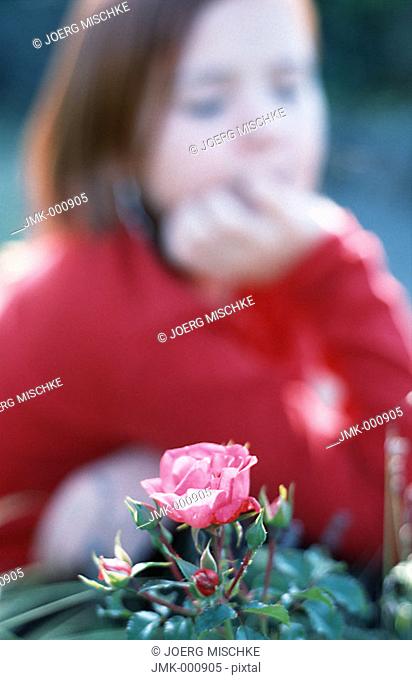 Little girl in the garden, looking at a rose