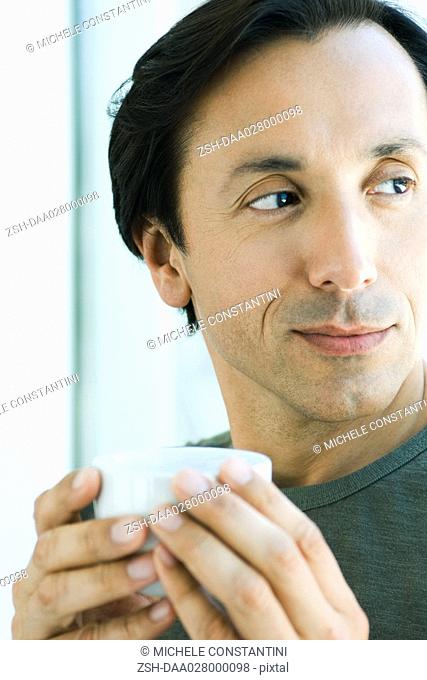 Mature man holding up cup, looking away, smiling