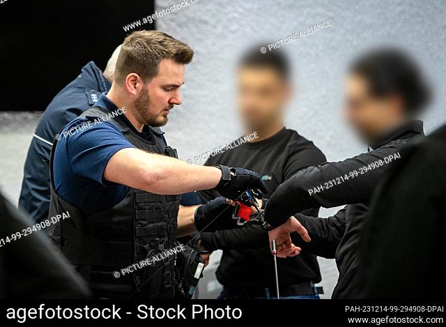 14 December 2023, Baden-Württemberg, Stuttgart: The handcuffs are removed from two of the five defendants in a courtroom at the regional court