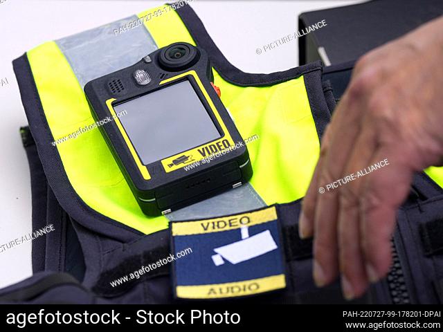 27 July 2022, Brandenburg, Potsdam: A hand reaches for the bodycam on a patrolman's protective vest lying on a table during a press event
