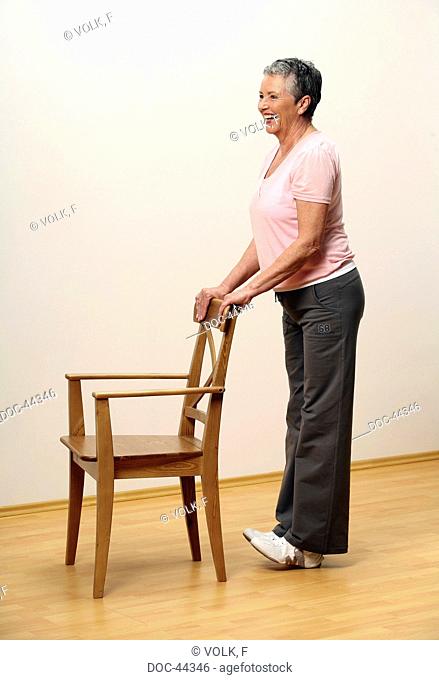 older woman doing gymnastics with a chair - woman is standing on her heels - pumping - muscularity - senior