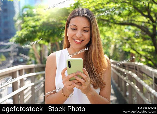Young beautiful woman using smartphone in a city. Smiling elegant girl texting on mobile phone outdoor. Modern lifestyle, connection, casual business concept