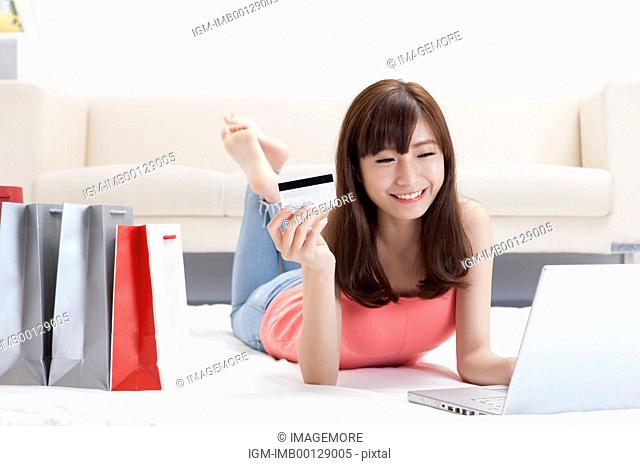 Young woman lying down on front and holding credit card with smile