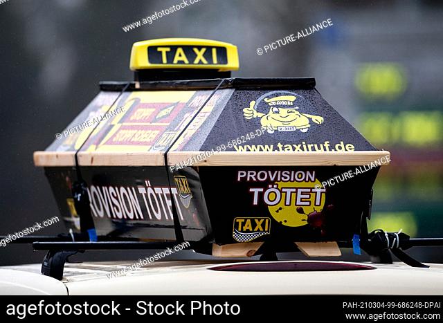 04 March 2021, North Rhine-Westphalia, Duesseldorf: A coffin with the inscription ""Provision Tötet"" is attached to the roof of a taxi during a demonstration