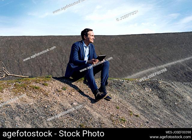 Mature businessman sitting on a disused mine tip holding tablet