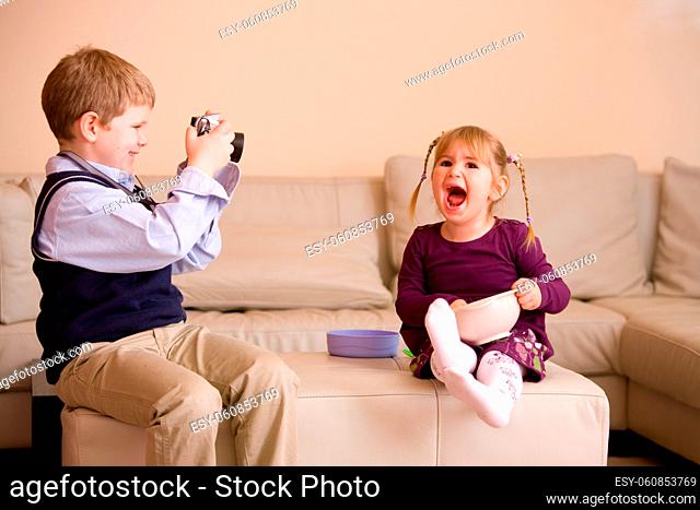 Young boy sitting on couch, taking a picture of his happy little sister
