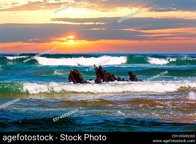 Sea surf waves and small rocks in center. Evening sunset seascape view from beach