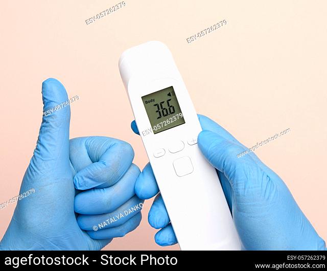 hands in blue latex gloves hold an electronic thermometer to measure temperature, non-contact device
