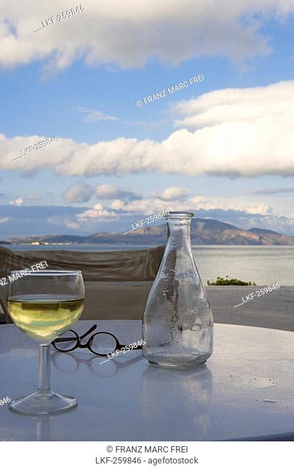 View over a wine glass and a carafe at coast area under clouded sky, Limni Keriou, Zakynthos, Ionian islands, Greece, Europe