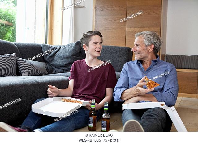 Father and son sitting on the floor eating pizza in living room