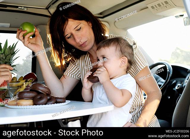 Beautiful woman looking at daughter eating donut while sitting in van during sunset