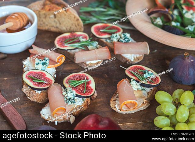 Easy diet salad with arugula, figs and blue cheese on a brown wooden surface. Sandwiches with ricotta, fresh figs, prosciutto, rosemary and blue cheese