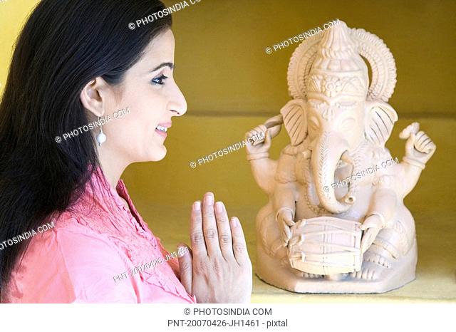 Side profile of a mid adult woman praying in front of a statue of God Ganesha