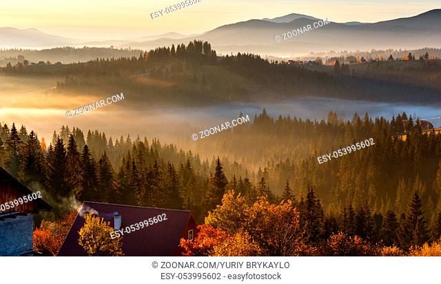 First sunrise rays of sun and shadows through fog and trees on slopes. Morning autumn Carpathian Mountains landscape (Yablunytsia village and pass