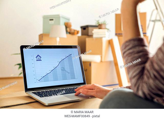 Woman using laptop with rising line graph on the screen in a new home