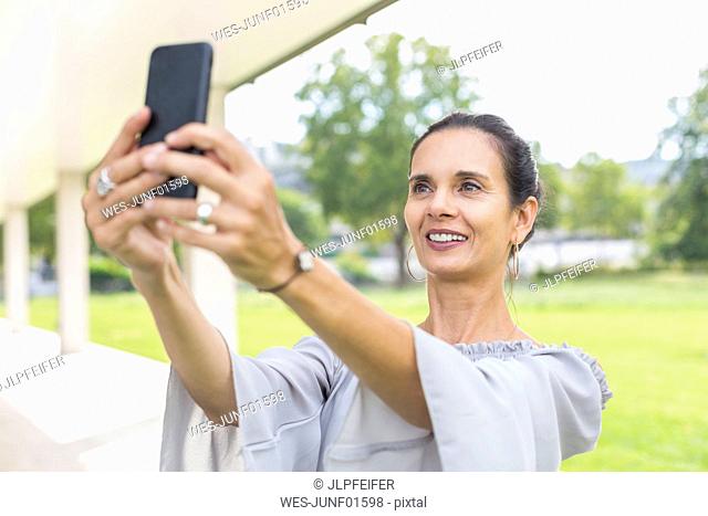 Portrait of smiling mature woman taking selfie with smartphone outdoors
