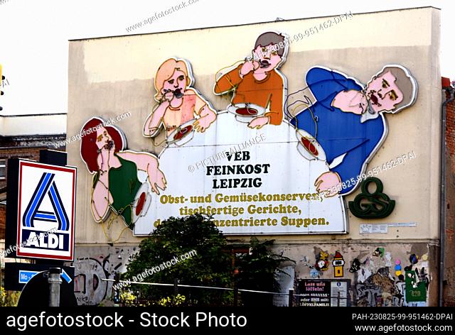 19 August 2023, Saxony, Leipzig: In front of the illuminated sign ""Löffelfamilie"" in Leipzig's Karl-Liebknecht-Strasse is an advertisement for the retail...