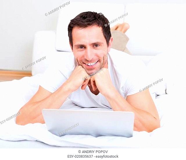 Portrait Of Young Man Lying On Bed Using Laptop