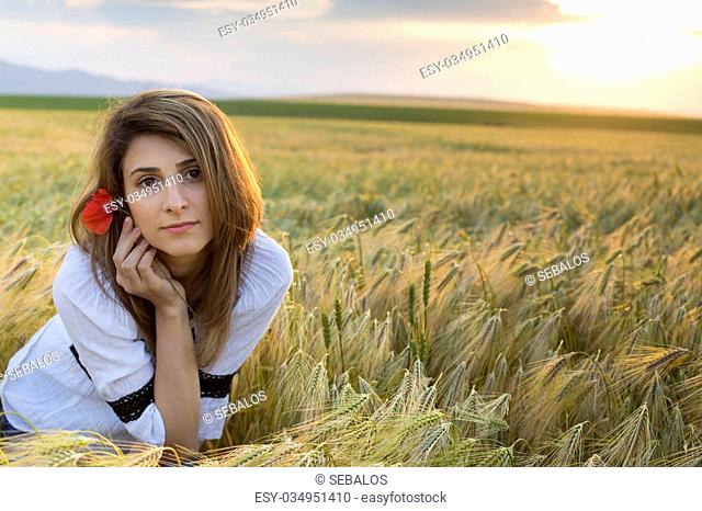 Young beautiful woman with poppy flower in wheat Field