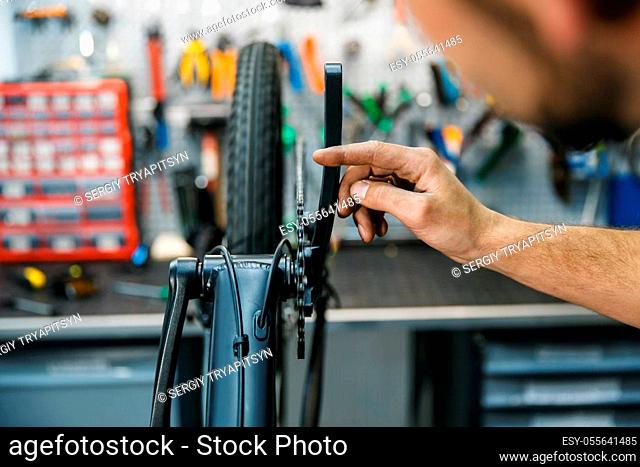 Bicycle assembly in workshop, man setting up a chain. Mechanic in uniform fix problems with cycle, professional bike repairing service