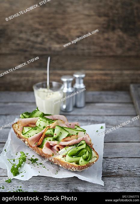 Baguette topped with cucumber and bacon on greaseproof paper