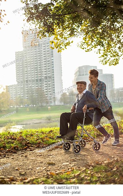 Grandson pushing happy senior man with wheeled walker
