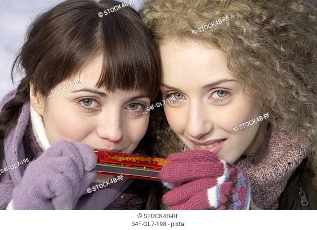 Two young women eating holding a harmonica, portrait