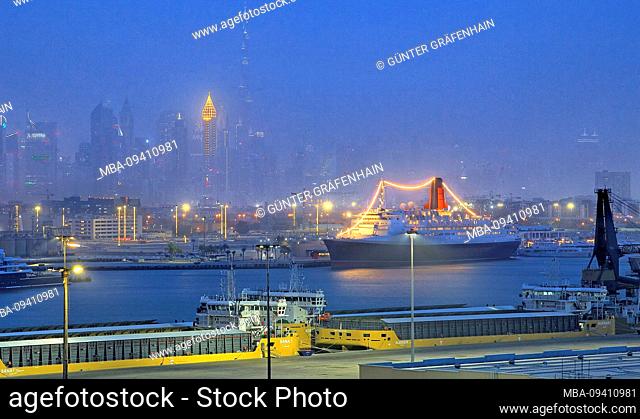 Hotel and museum ship Queen Elizabeth 2 (QE2) in the harbor with city skyline and Burj Khalifa 828m at night, Dubai, Persian Gulf, United Arab Emirates