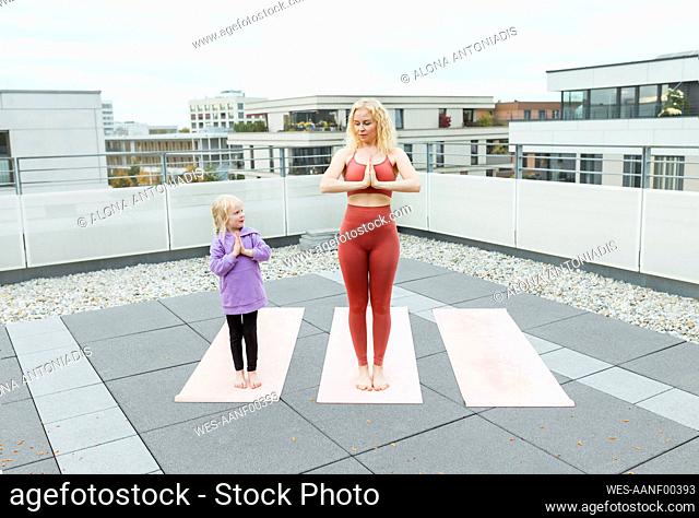 Cute girl practicing yoga with mother on rooftop