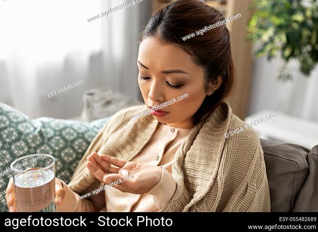 sick asian woman with medicine and water at home
