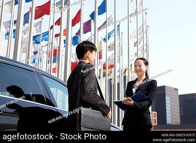 Two businesspeople meeting outdoors with flagpoles in background