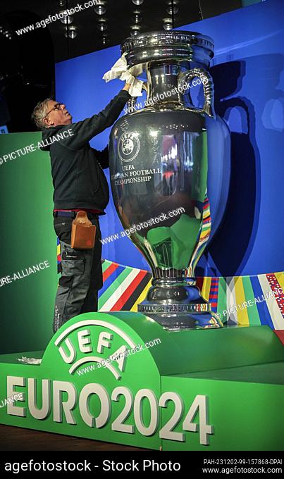 02 December 2023, Hamburg: Soccer: European Championship, draw - preliminary round in Hamburg, Elbphilharmonie. A man cleans an oversized trophy on the plaza...